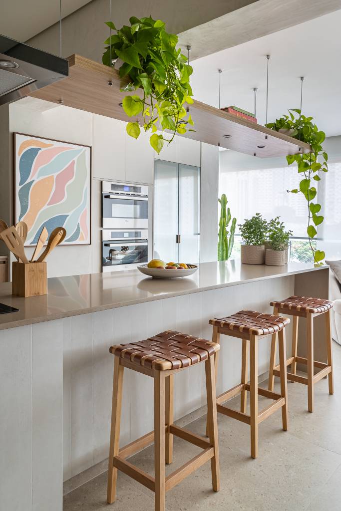 Apê ganha ilha de cozinha espaçosa e brises delimitando sala de TV. Projeto de Go Up Arquitetura. Na foto, cozinha integrada, plantas suspensas.