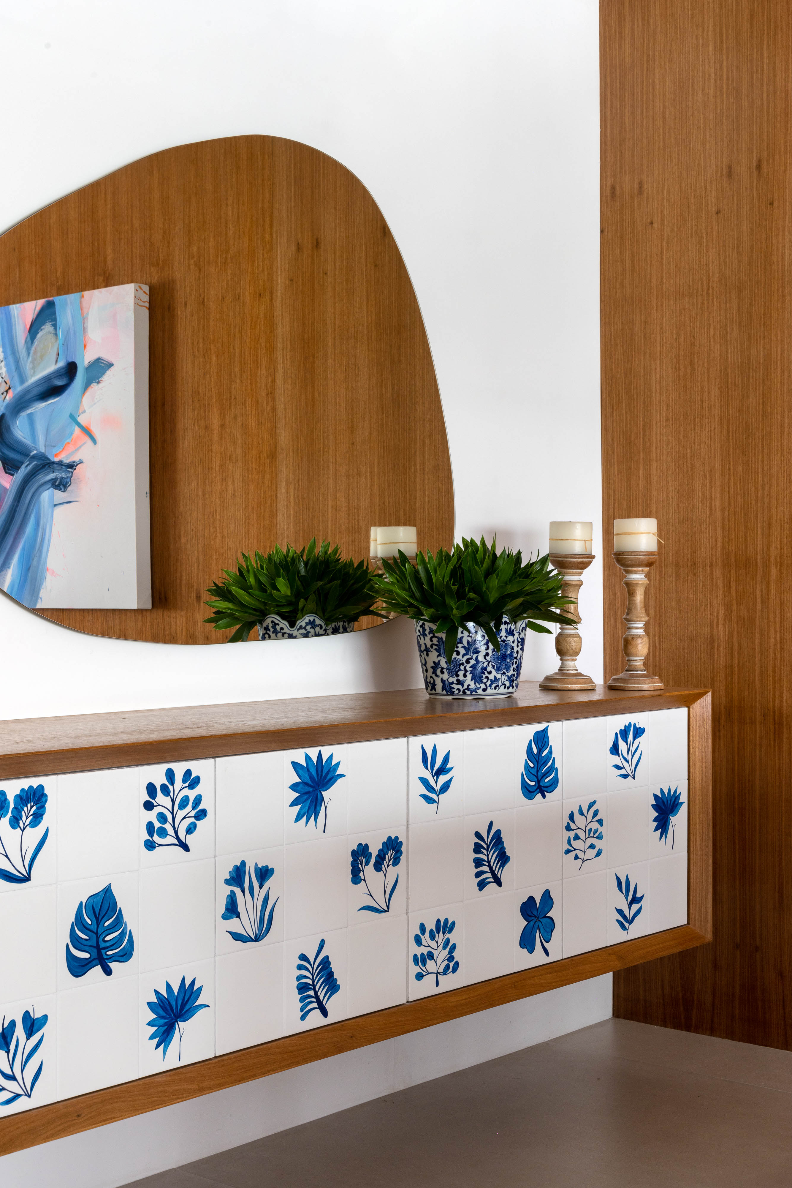Azulejos pintados à mão com estampas botânicas revestem varanda de apê. Projeto de Renata Lemos. Na foto, buffet com azulejos, espelho em forma orgânica.