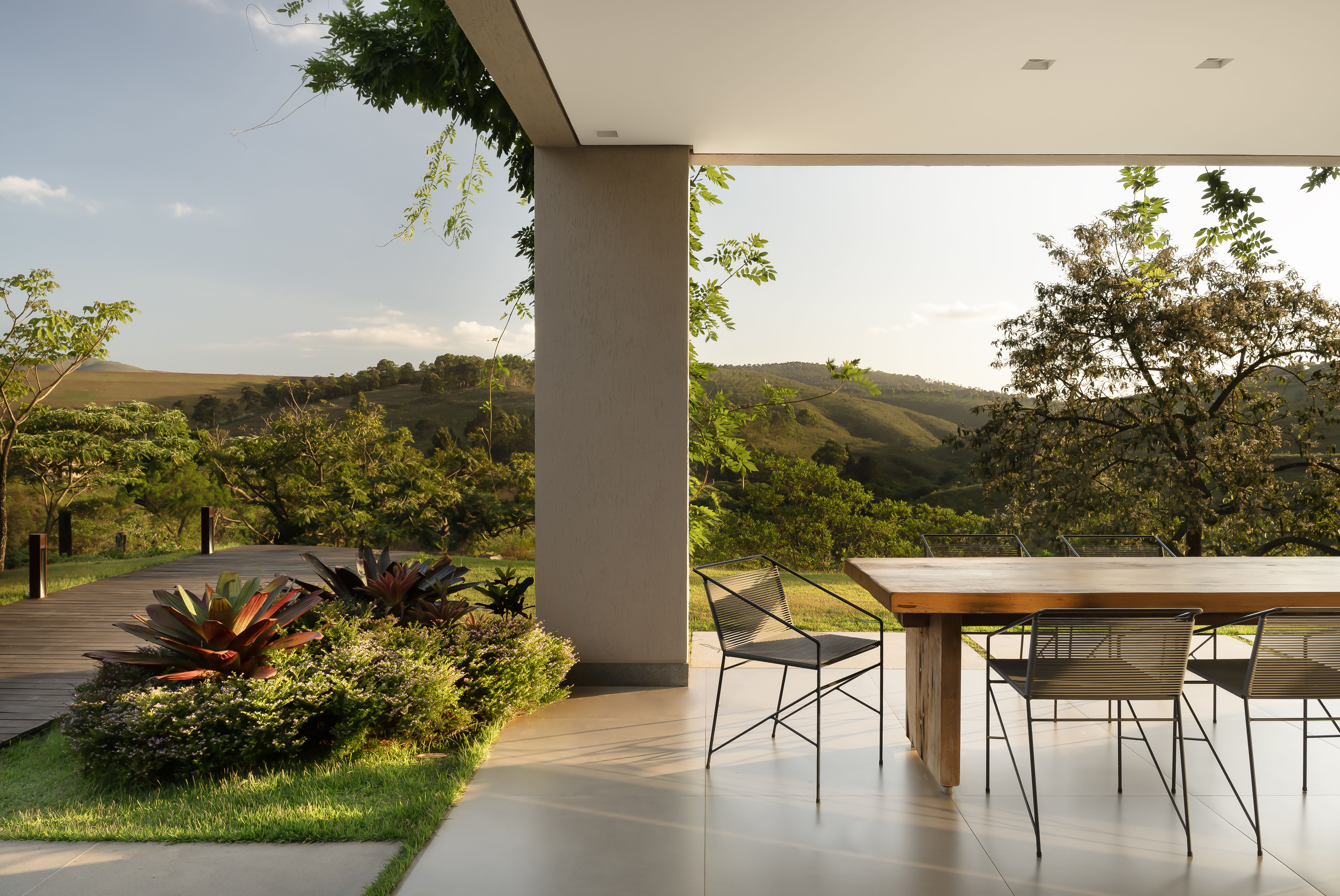 Sintonia com natureza: casa de campo com lareira tem sofá e cozinhas roxos. Projeto de Camila Medrado. Na foto, varanda, jardim, mesa, cadeiras.