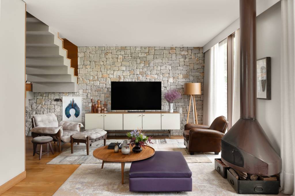 Sintonia com natureza: casa de campo com lareira tem sofá e cozinhas roxos