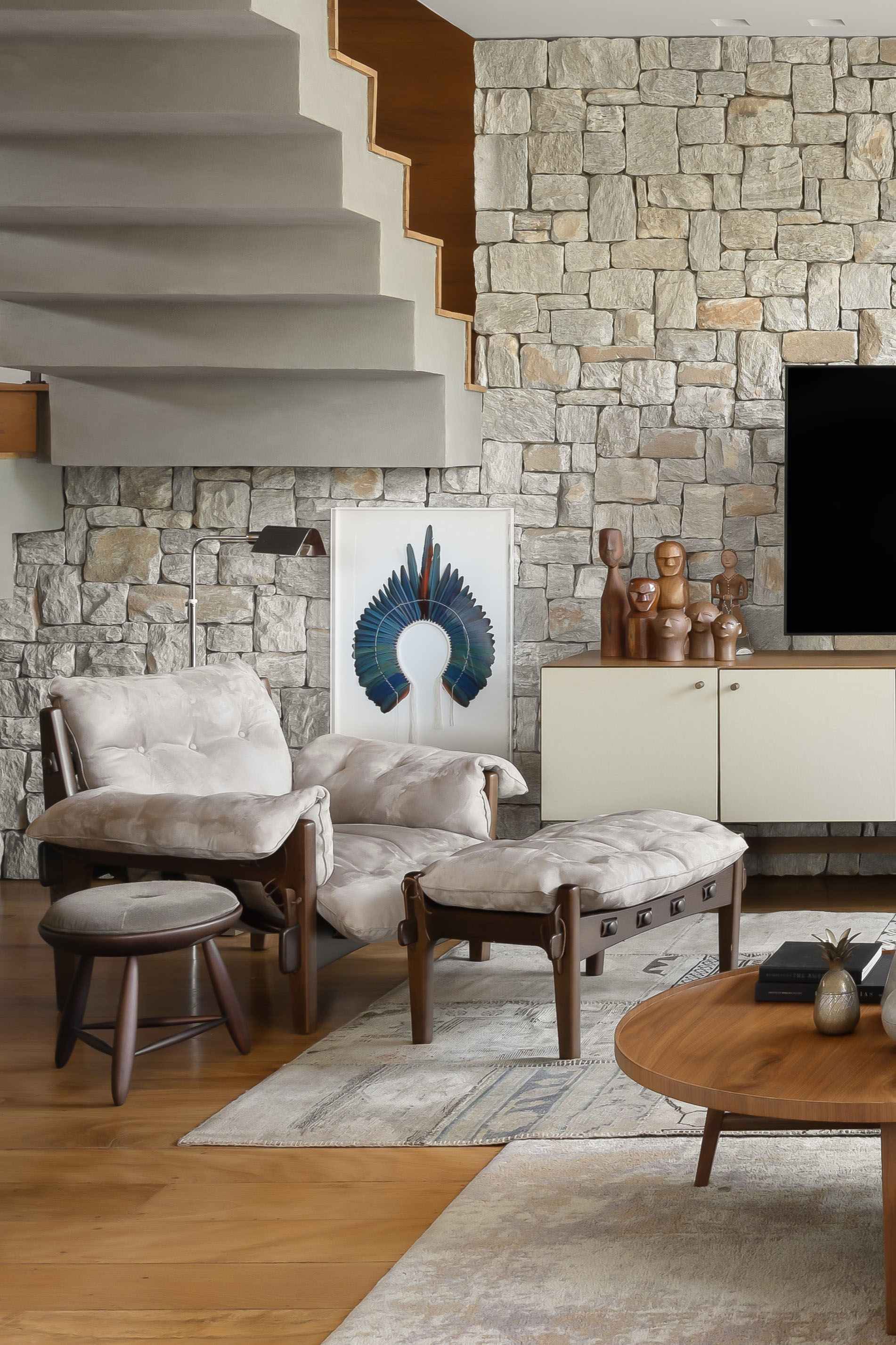 Sintonia com natureza: casa de campo com lareira tem sofá e cozinhas roxos. Projeto de Camila Medrado. Na foto, sala de estar, poltrona com pufe, parede de pedras.