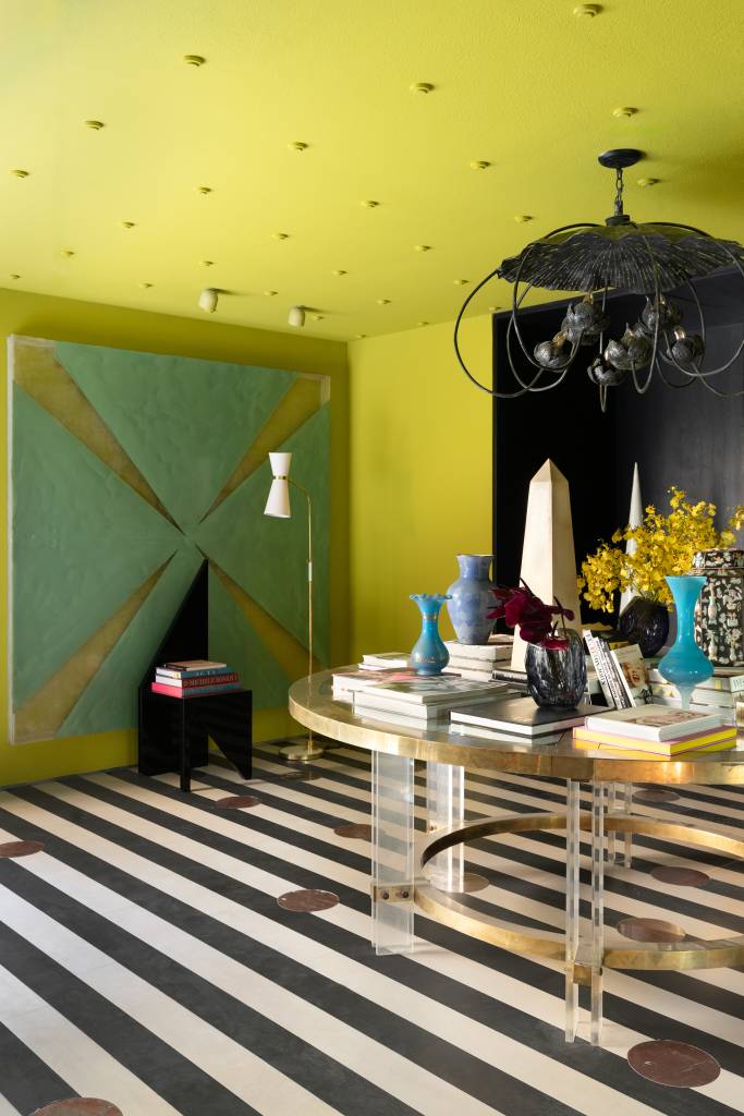 CASACOR São Paulo: hall maximalista tem parede espelhada e piso listrado. Projeto de Gustavo Scaramella. Na foto, hall com mesa de centro e lustre de destaque