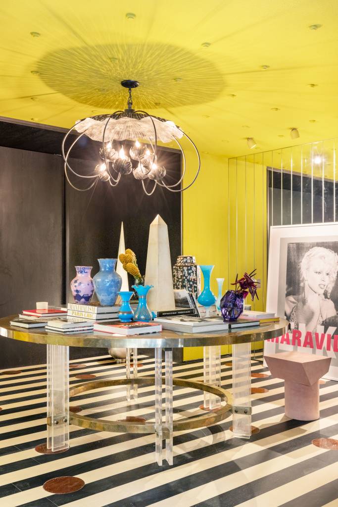 CASACOR São Paulo: hall maximalista tem parede espelhada e piso listrado. Projeto de Gustavo Scaramella. Na foto, mesa de centro com peças decorativas e lustre de destaque