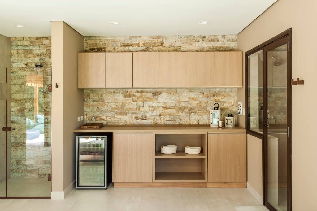 Cores naturais: veja quais são os tons mais populares com projetos e dicas. Projeto de Korman Arquitetos. Na foto, cozinha com marcenaria bege e parede de pedras.
