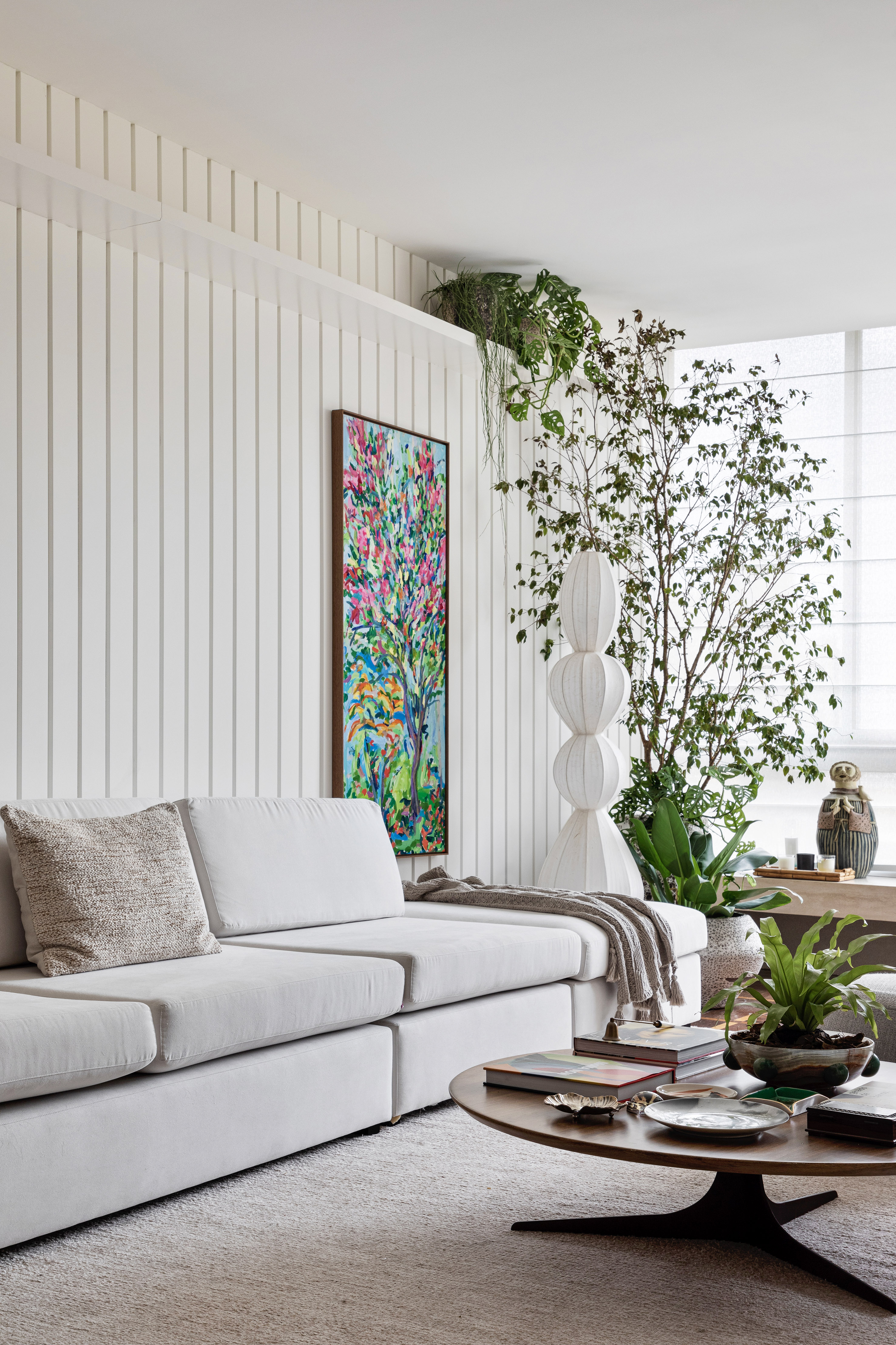 Farm house com toque boho e moderno: apê de 200 m² mescla estilos. Projeto de Rebeca de França. Na foto, sala de estar, parede de lambri branca, sofá branco, árvore.