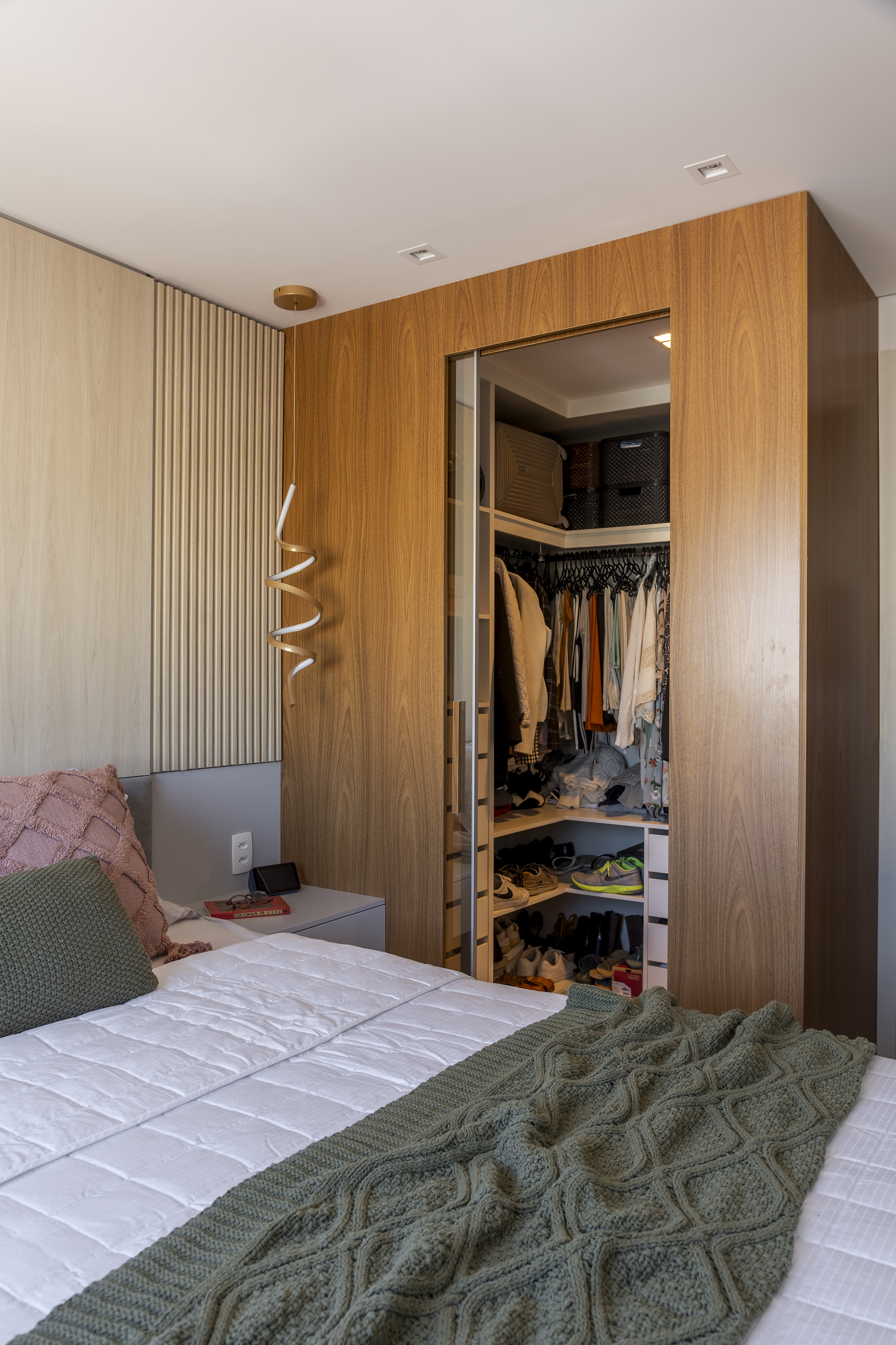 Funkos e livros ganham destaque em reforma de apê de 64 m². Projeto de Vitoria Lacerda. Na foto, quarto com painel de madeira clara ripada, closet.