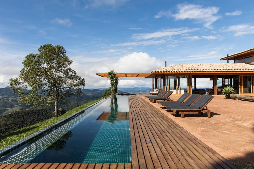 Linda casa na montanha tem lareira e cozinha rústica com fogão à lenha. Projeto de Sabella Arquitetura. Na foto, piscina, deck.