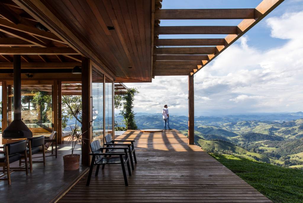 Linda casa na montanha tem lareira e cozinha rústica com fogão à lenha. Projeto de Sabella Arquitetura. Na foto, varanda, deck, vista.