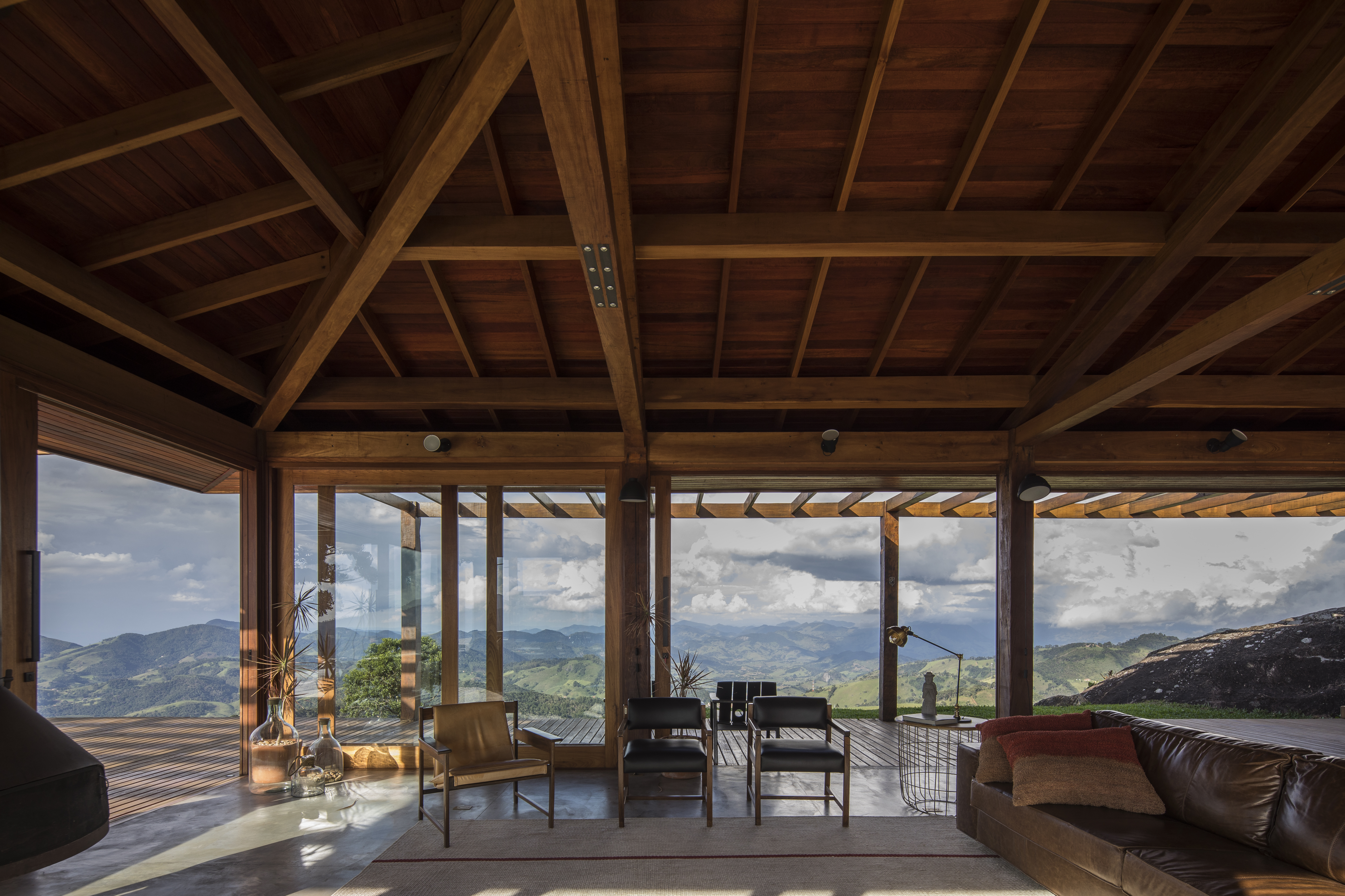 Linda casa na montanha tem lareira e cozinha rústica com fogão à lenha. Projeto de Sabella Arquitetura. Na foto, sala de estar, vista para montanha.