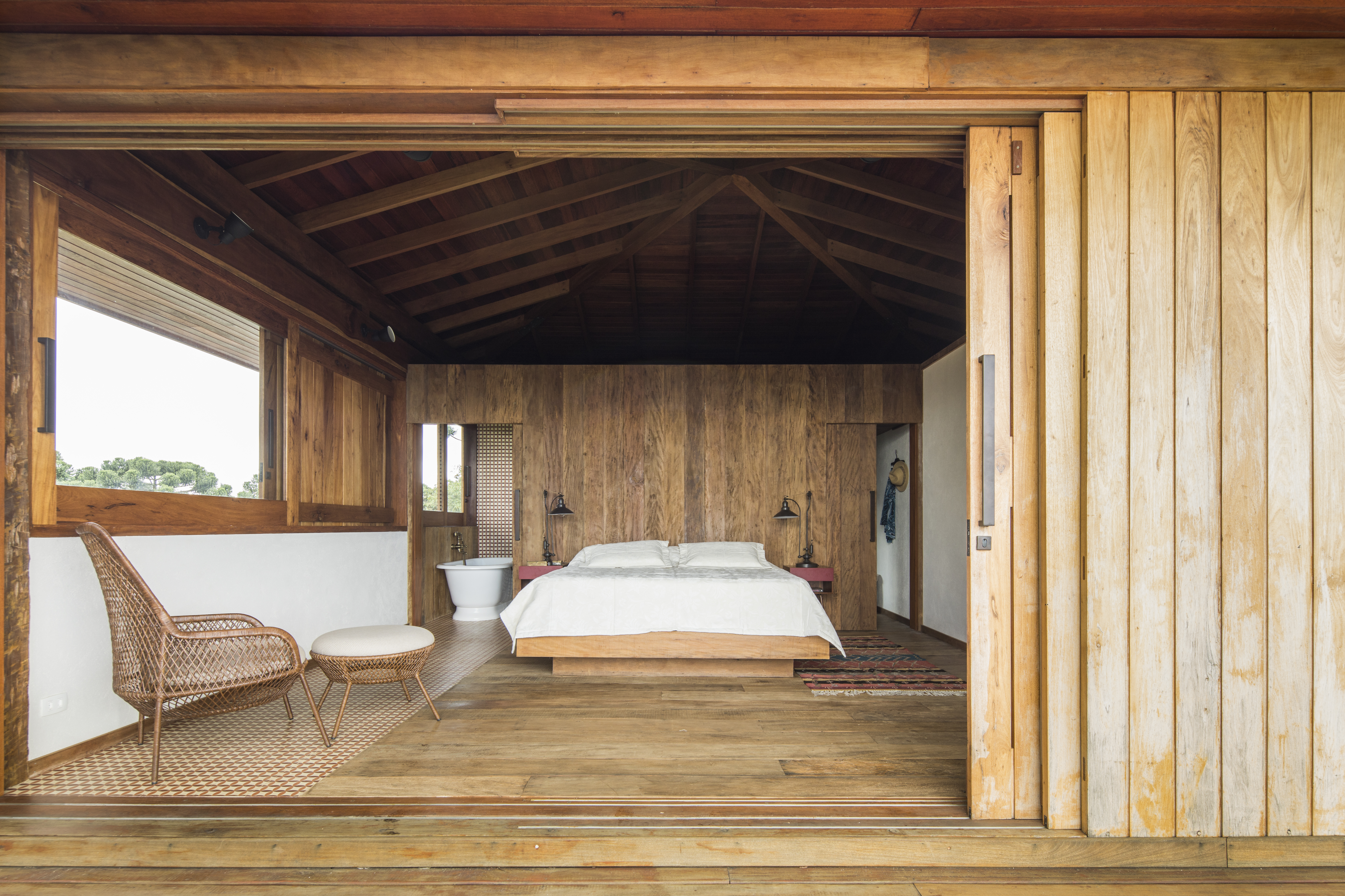 Linda casa na montanha tem lareira e cozinha rústica com fogão à lenha. Projeto de Sabella Arquitetura. Na foto, quarto rústico, piso e parede de madeira.