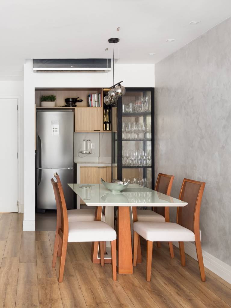 Parede entre sala e cozinha é demolida é dá lugar à cristaleira neste apê. Projeto de MA.DÊ Arquitetura. Na foto, sala de jantar, cimento queimado, mesa com tampo branco.