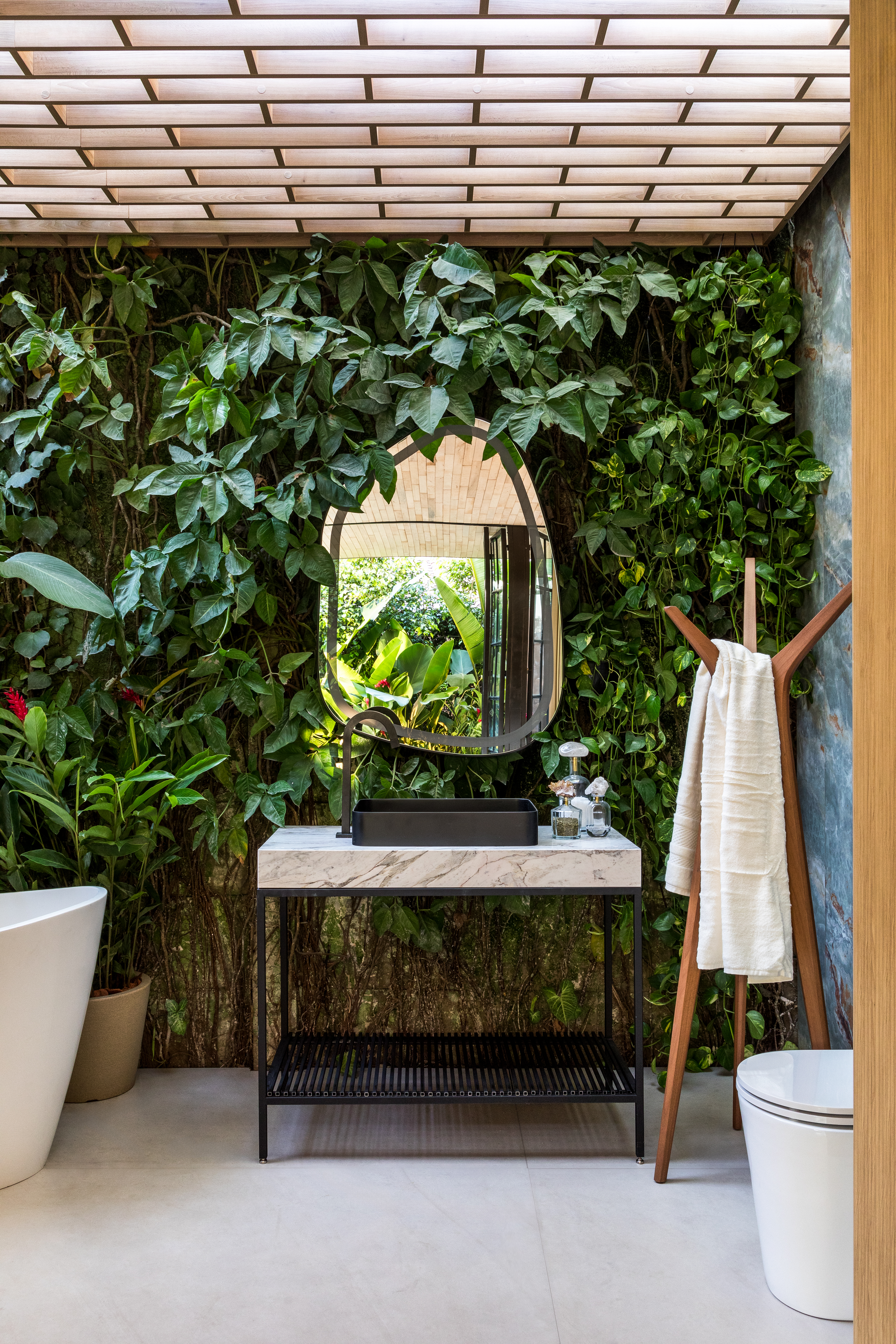 Pedras e vegetação em abundância marcam a estética orgânica deste loft. Projeto de Maria Alice Crippa e Gustavo Assis. Na foto, banheiro com parede viva e espelho em formato orgânico