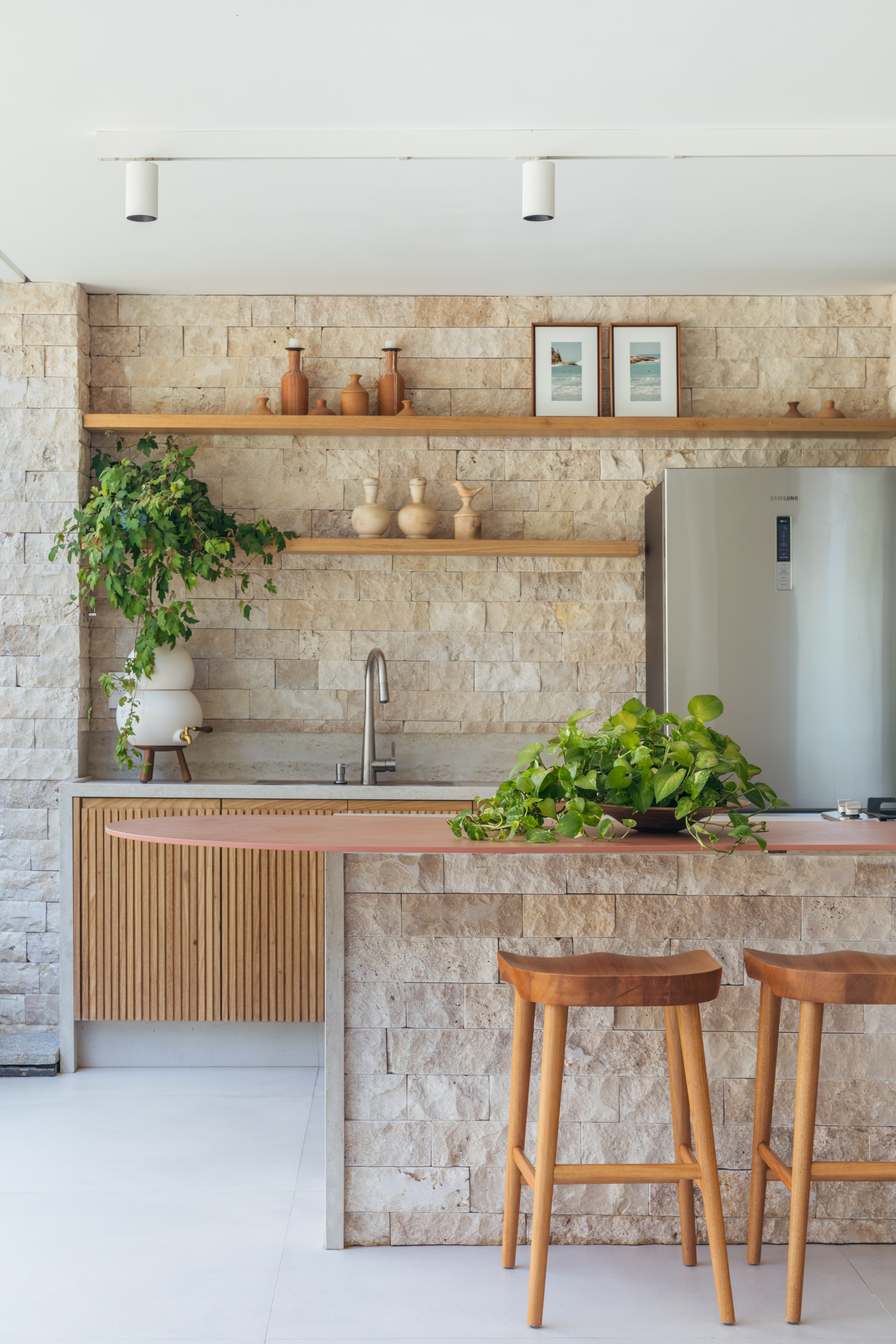 Pergolados com forro em fibras de bambu trançadas envolvem casa de 195 m². Projeto de Amanda Miranda. Na foto, área gourmet, parede de pedra, plantas.