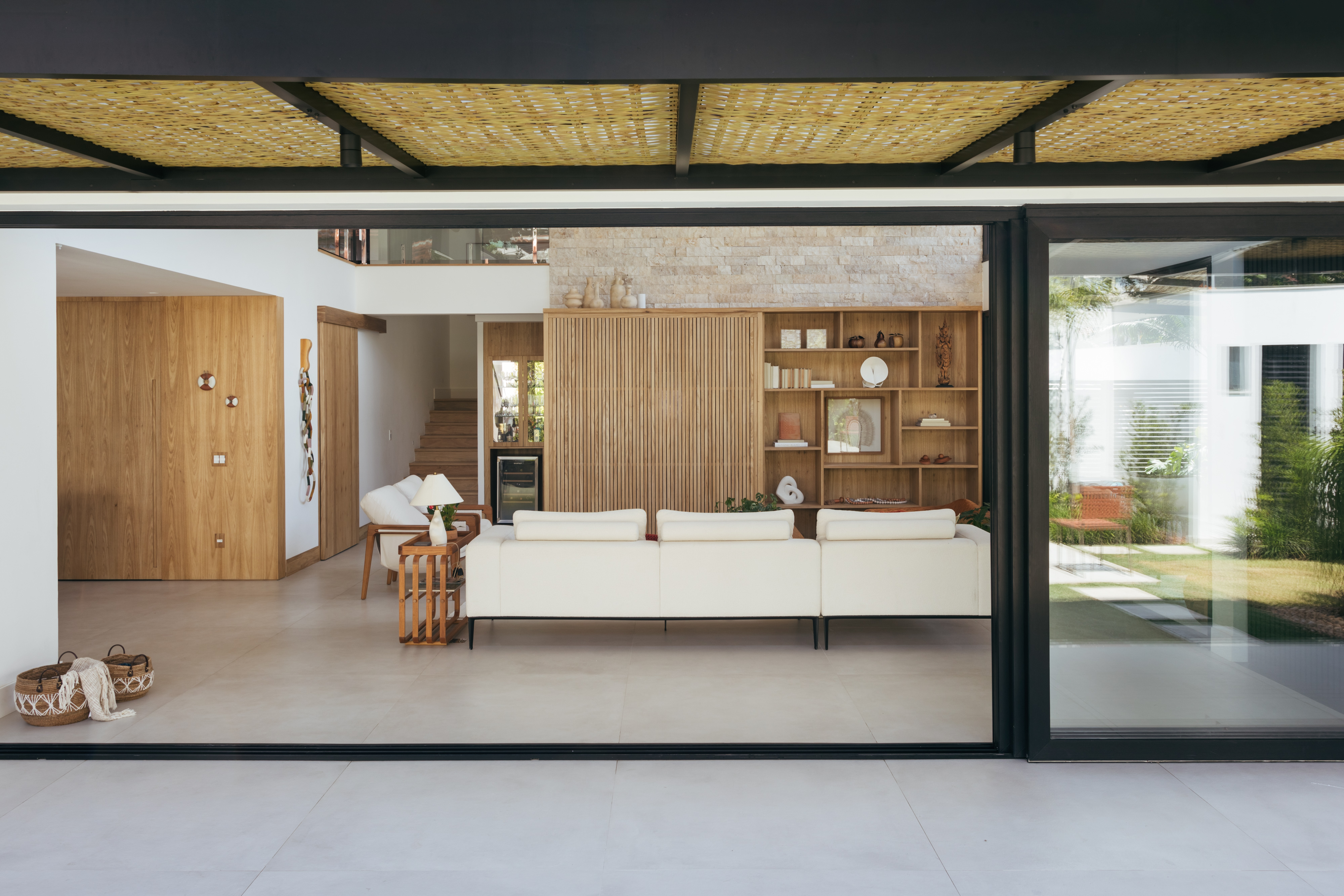 Pergolados com forro em fibras de bambu trançadas envolvem casa de 195 m². Projeto de Amanda Miranda. Na foto, sala de estar, portas de vidro,