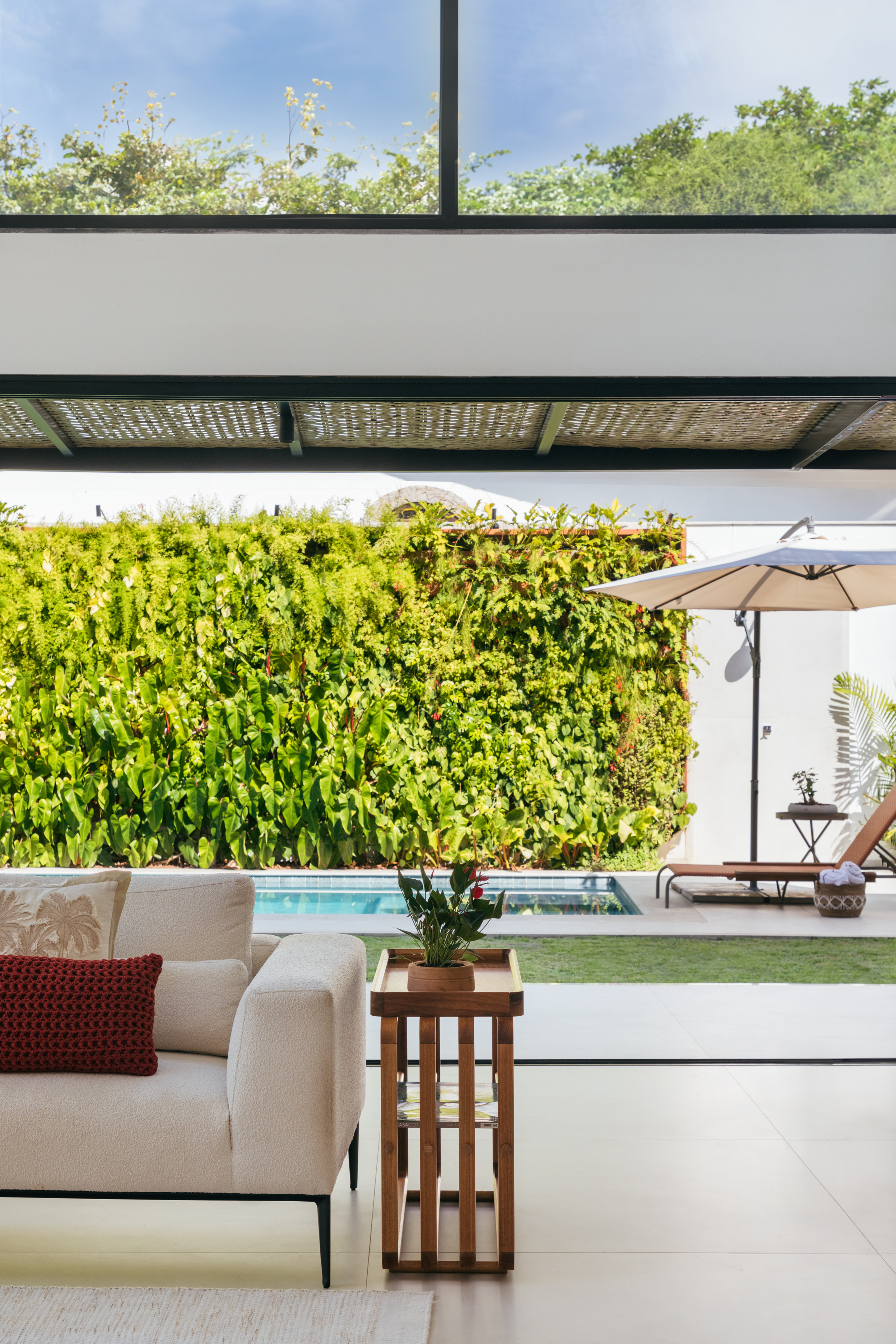 Pergolados com forro em fibras de bambu trançadas envolvem casa de 195 m². Projeto de Amanda Miranda. Na foto, área externa, jardim vertical, piscina.