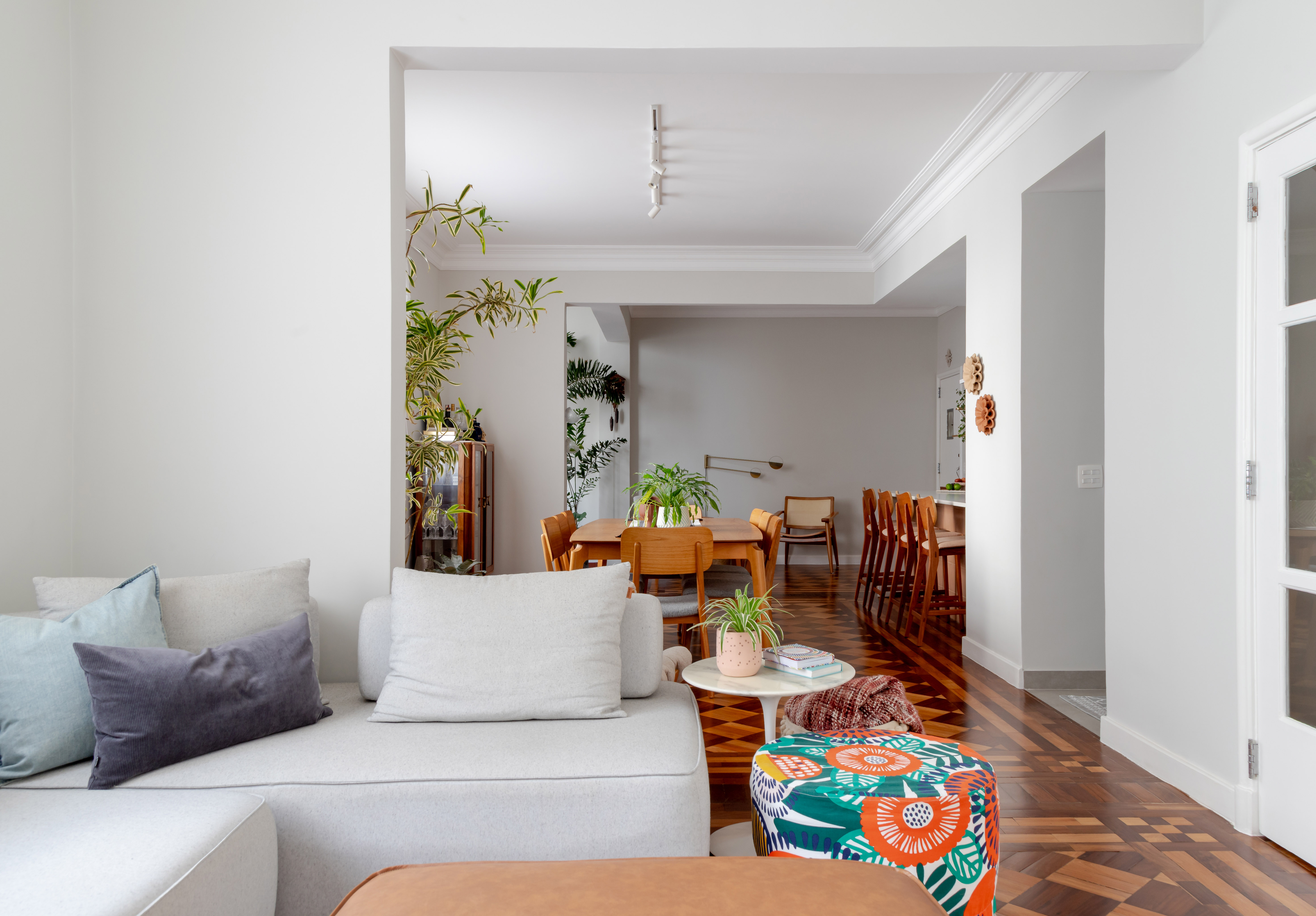 Piso de taco, janelas brancas e sancas dão charme parisiense a este apê. Projeto de Ana Paula Crivelenti. Na foto, sala de estar, pufes, sofá cinza claro.