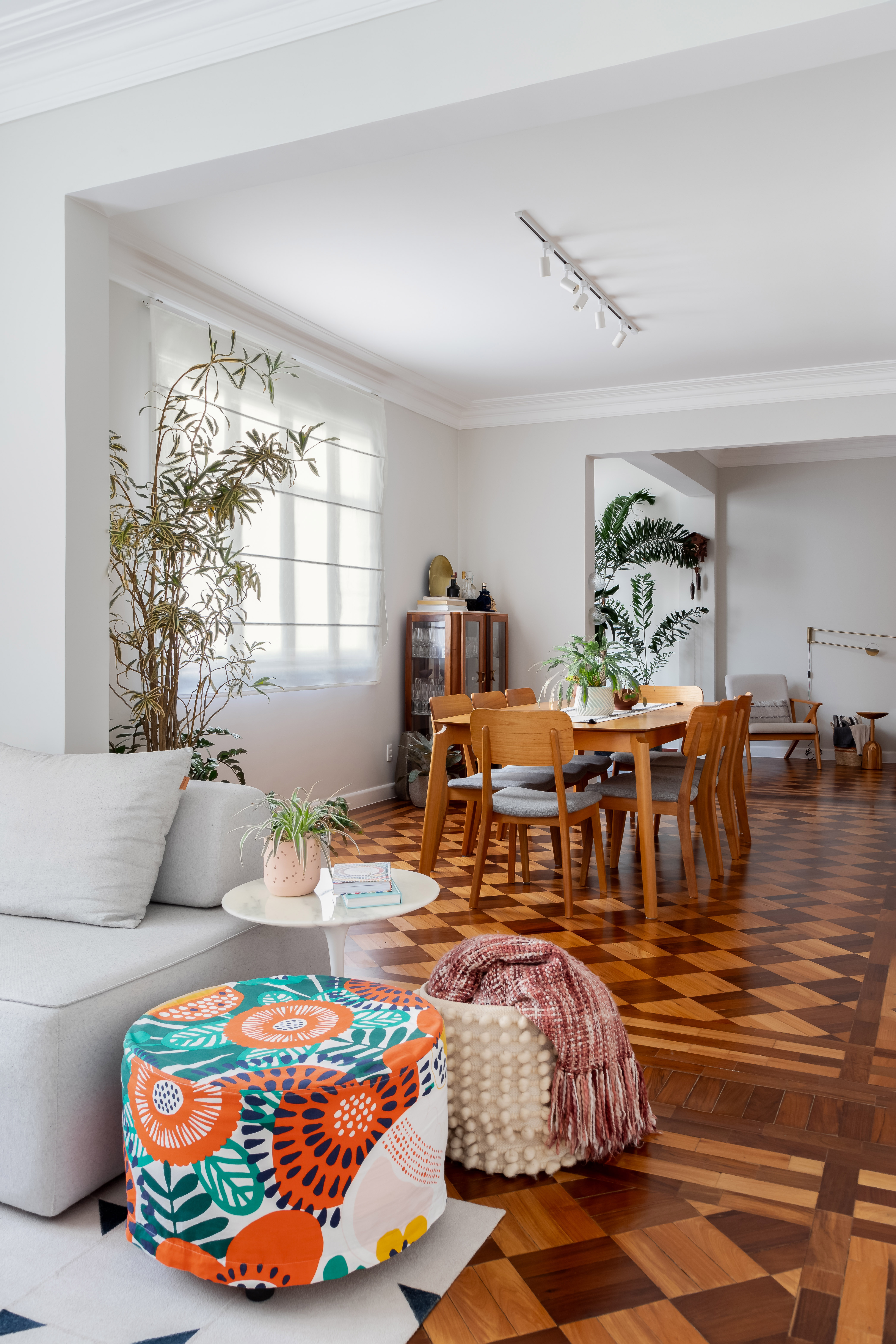 Piso de taco, janelas brancas e sancas dão charme parisiense a este apê. Projeto de Ana Paula Crivelenti. Na foto, sala de estar, pufe colorido, sofá cinza claro.