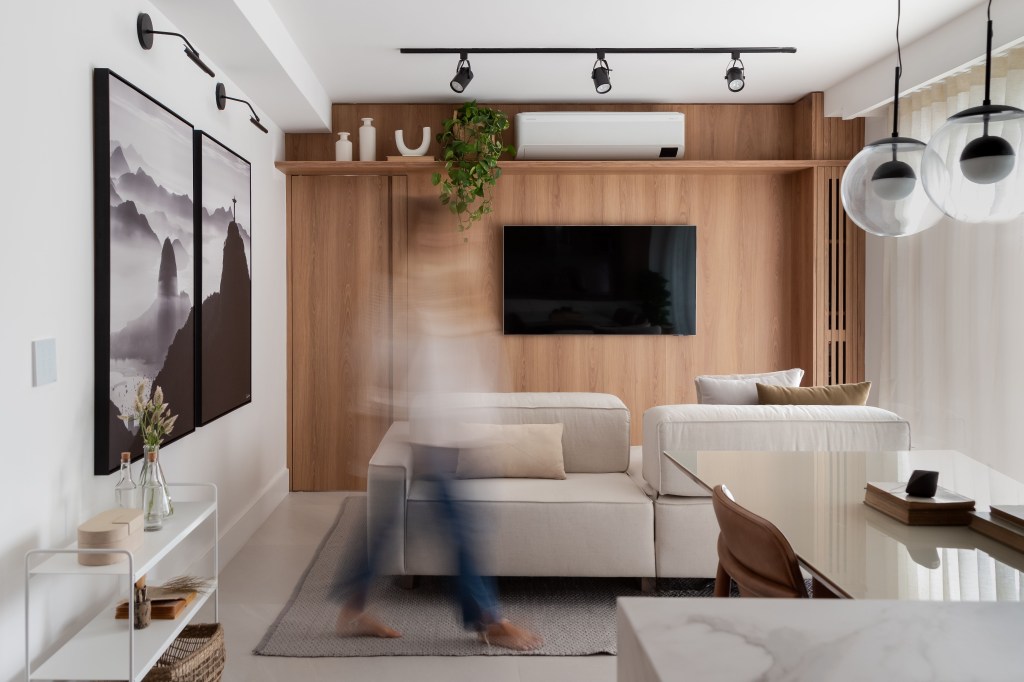 Reforma em apê de 73 m² cria mini lavabo com paredes de drywall. Projeto de Casa Tauari. Na foto, sala de estar, painel de madeira com tv, sofá off white.