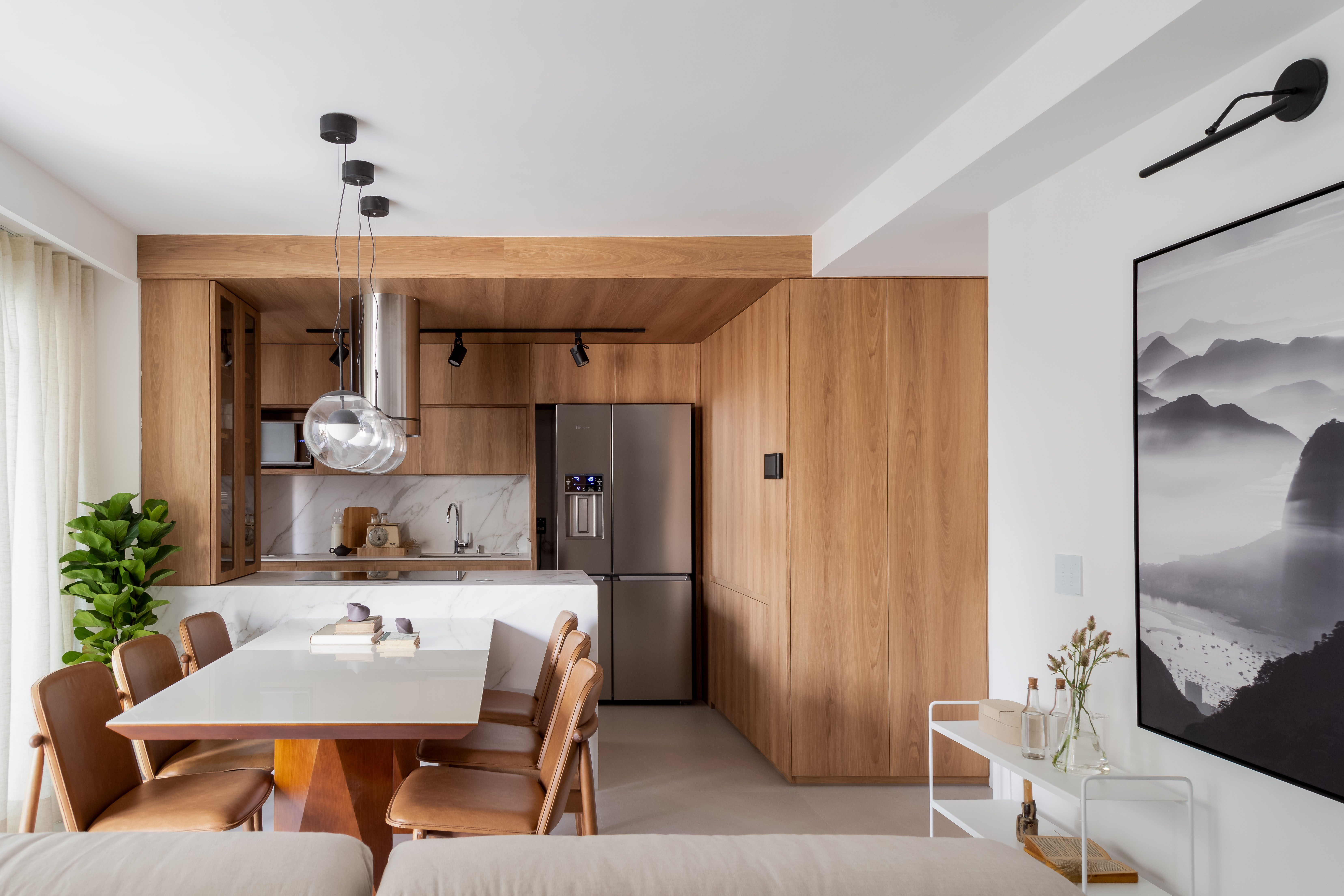 Reforma em apê de 73 m² cria mini lavabo com paredes de drywall. Projeto de Casa Tauari. Na foto, cozinha integrada com sala, paredes revestidas com painéis de madeira, bancada branca com mesa de jantar.