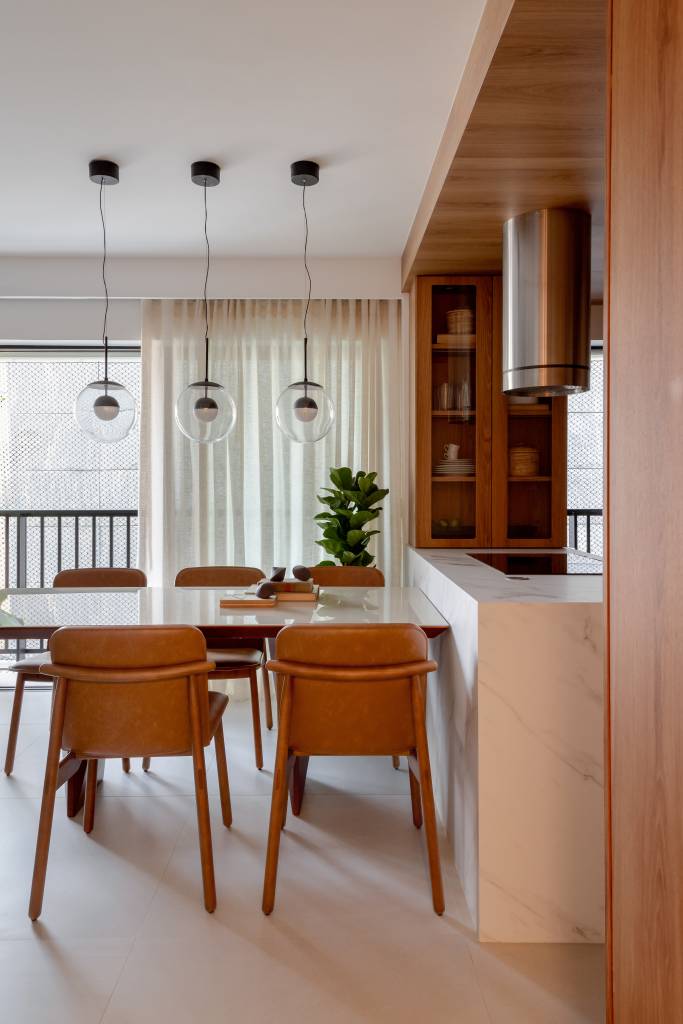 Reforma em apê de 73 m² cria mini lavabo com paredes de drywall. Projeto de Casa Tauari. Na foto, cozinha integrada com sala, paredes revestidas com painéis de madeira, bancada branca com mesa de jantar.