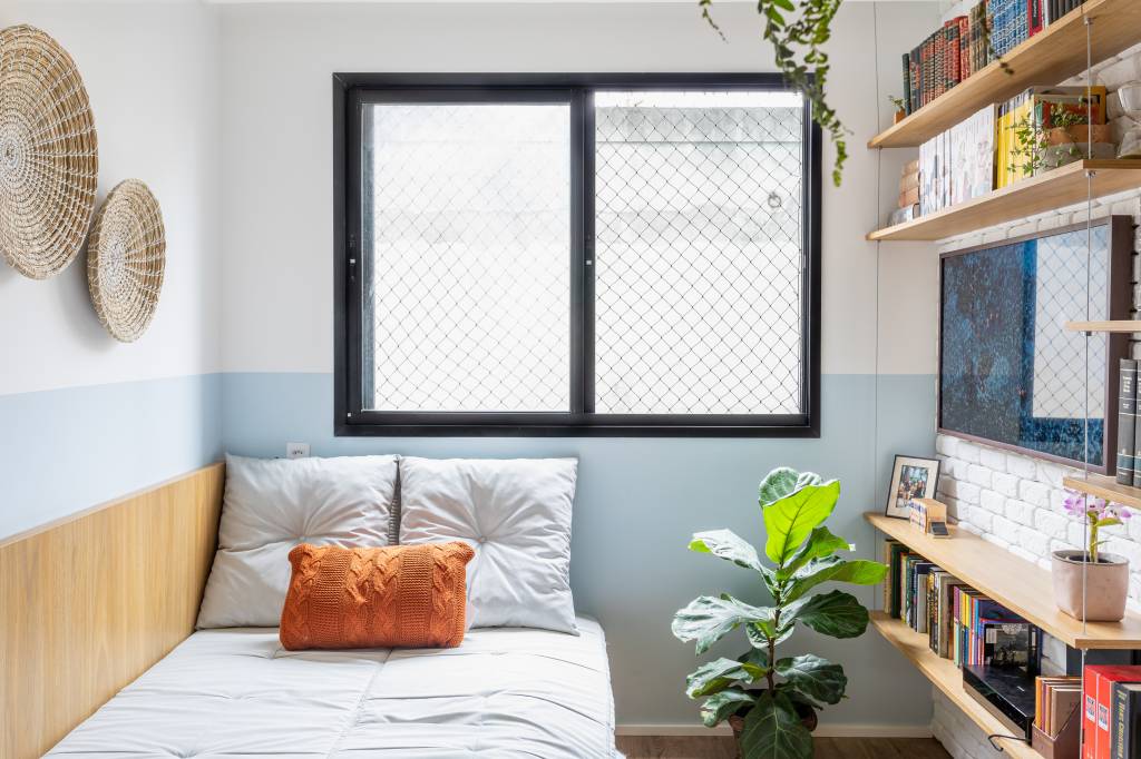 Miniapê de 25 m² tem sofá de canto alemão com baú e estante de mil livros. Projeto de Lemarchi Arquitetura. Na foto, sala, cestos na parede, meia parede azul.