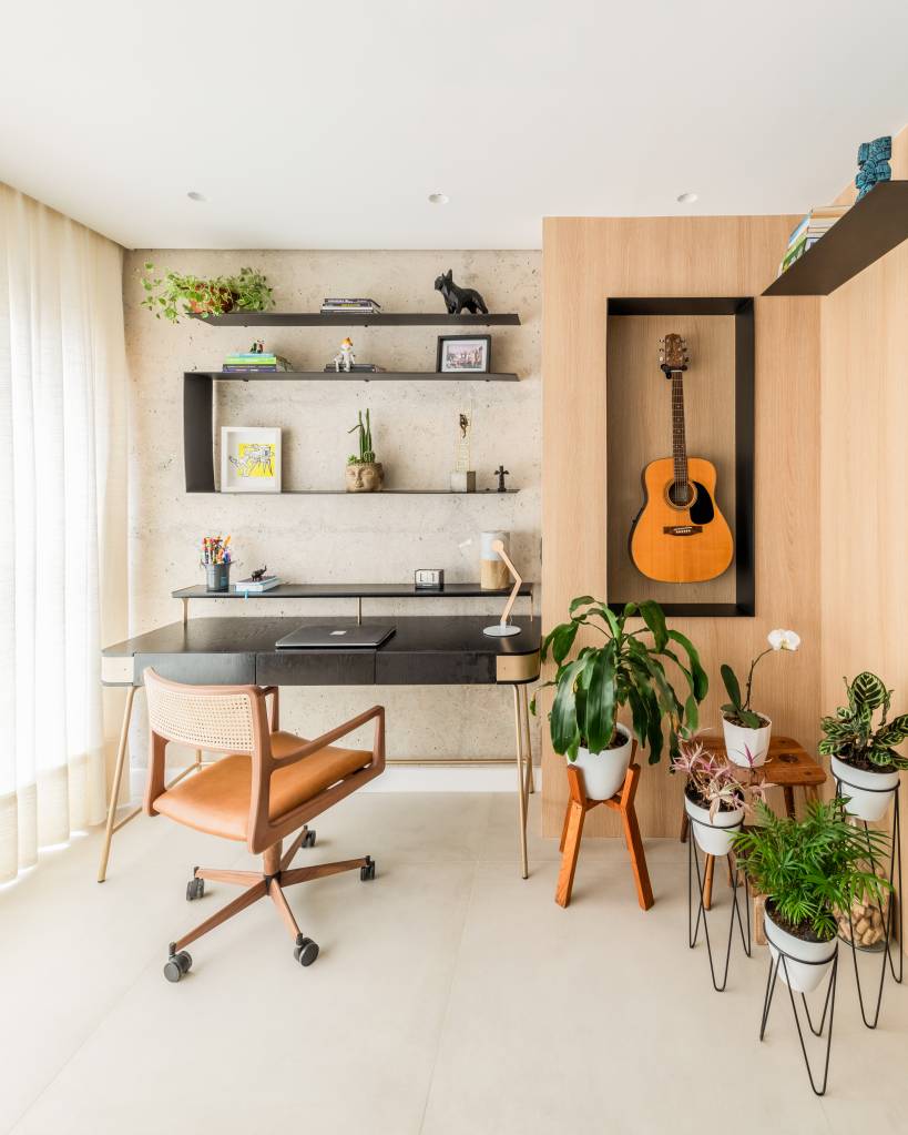 Bancada de lâmina sintetizada integra cozinha e área gourmet neste apartamento. Projeto de BMA Studio. Na foto, home office, nicho para violão, plantas.