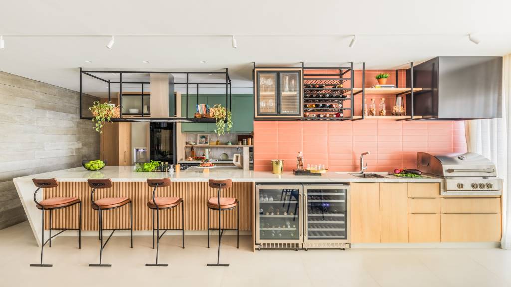 Bancada de lâmina sintetizada integra cozinha e área gourmet neste apartamento. Projeto de BMA Studio. Na foto, cozinha, backsplash de azulejos peach fuzz, salmão, prateleiras aéreas.