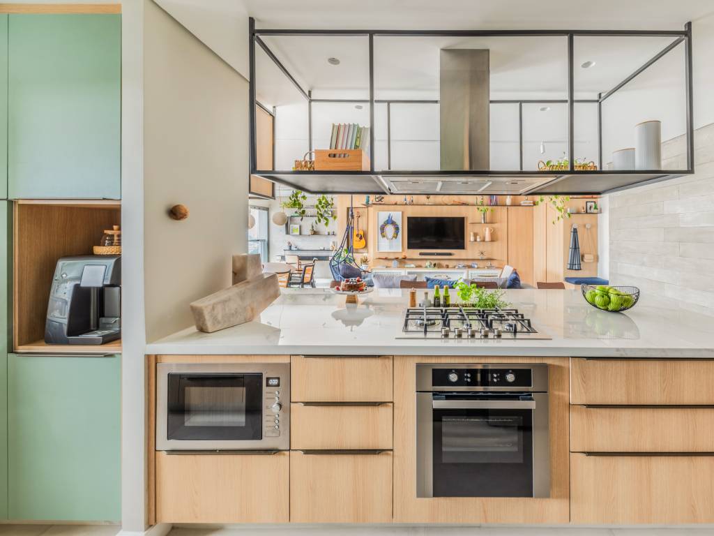 Bancada de lâmina sintetizada integra cozinha e área gourmet neste apartamento. Projeto de BMA Studio. Na foto, cozinha integrada, marcenaria verde.