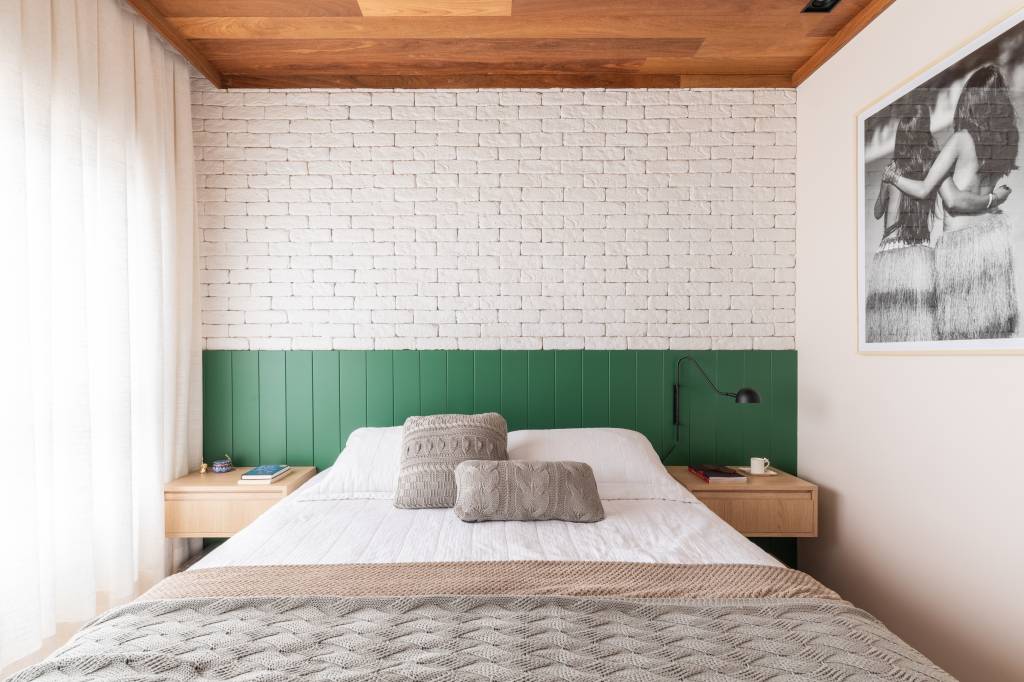 Bancada de lâmina sintetizada integra cozinha e área gourmet neste apartamento. Projeto de BMA Studio. Na foto, quarto de casal, cabeceira em lambri verde, parede de tijolinhos brancos.