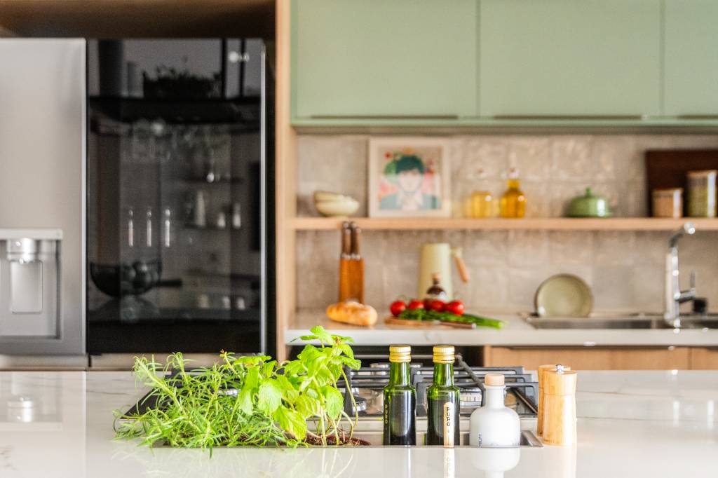 Bancada de lâmina sintetizada integra cozinha e área gourmet neste apartamento. Projeto de BMA Studio. Na foto, bancada de cozinha, espaço para horta pequena, armário verde.