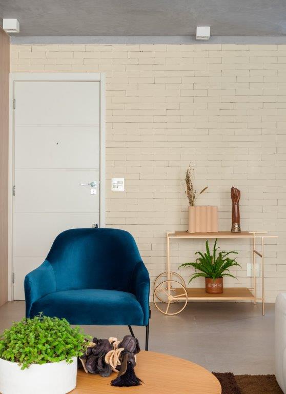 Closet integrado com sala de banho é o destaque de apê de 100 m². Projeto de Blaia e Moura Arquitetura. Na foto, sala de estar, poltrona azul, carrinho de chá, parede de tijolinhos.