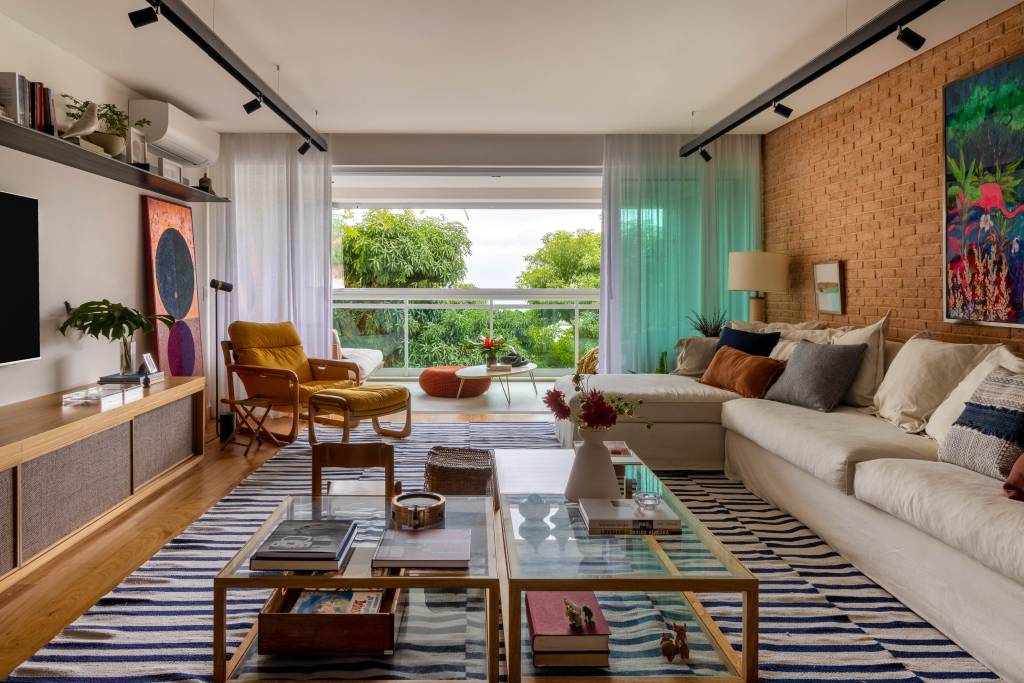 Cozinha de apê tem armário verde oliva, azulejo branco e paredes com toque preto. Projeto de Escala Arquitetura. Na foto, sala de estar, mesa de centro com tampo de vidro, tapete azul e branco, sofá branco, tijolinhos.