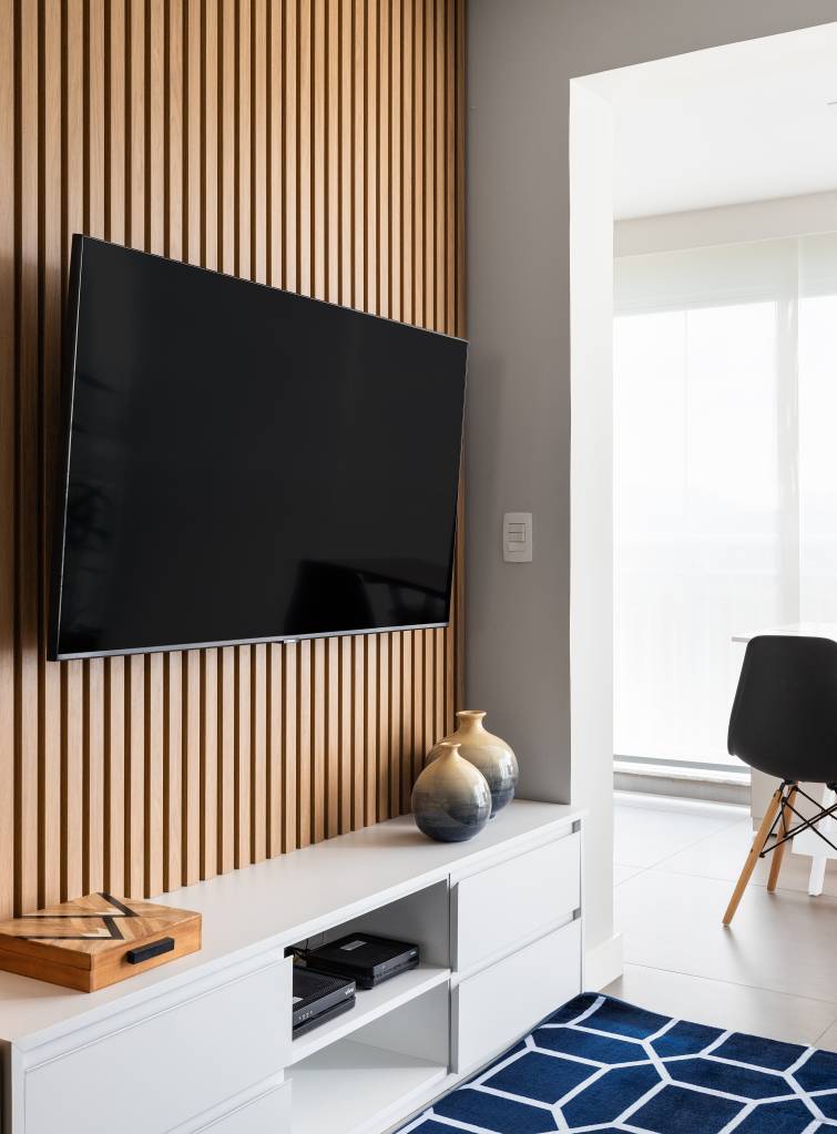 Cozinha com gabinete azul e painel ripado na sala dão textura e cor a apê de 62 m². Projeto de Duno Arquitetura. Na foto, sala de tv, tapete azul, rack branco.