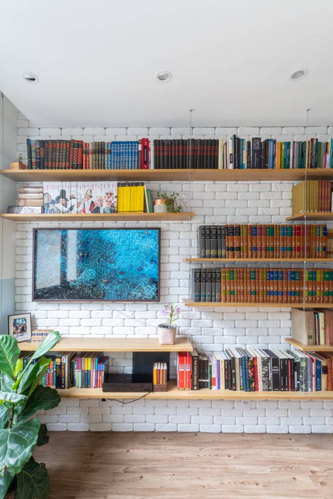 Miniapê de 25 m² tem sofá de canto alemão com baú e estante de mil livros. Projeto de Lemarchi Arquitetura. Na foto, prateleiras com livros, parede de tijolinhos.