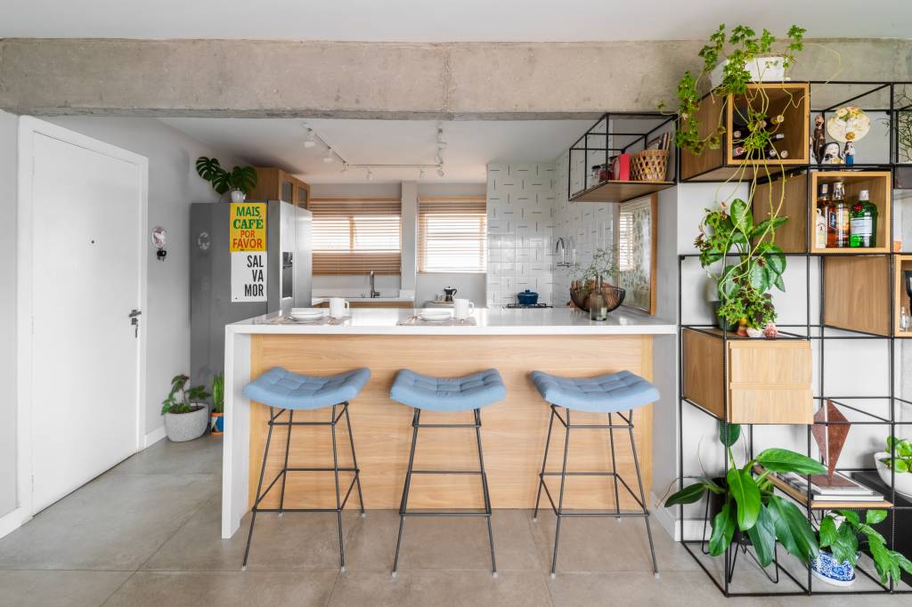 Pisos: guia para escolher o melhor material para cozinha, sala, quarto e banheiro. Projeto de BMA Studio. Na foto, cozinha integrada, banquetas azuis, vigas de concreto, plantas.