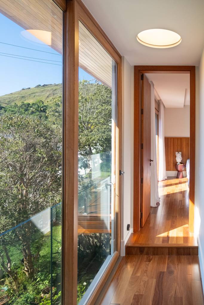 Linda casa de 800 m² tem área gourmet, piscina, sauna e terraço para contemplar o mar. Projeto de Viviane Cunha. Na foto, corredor com grandes lâminas de vidro.