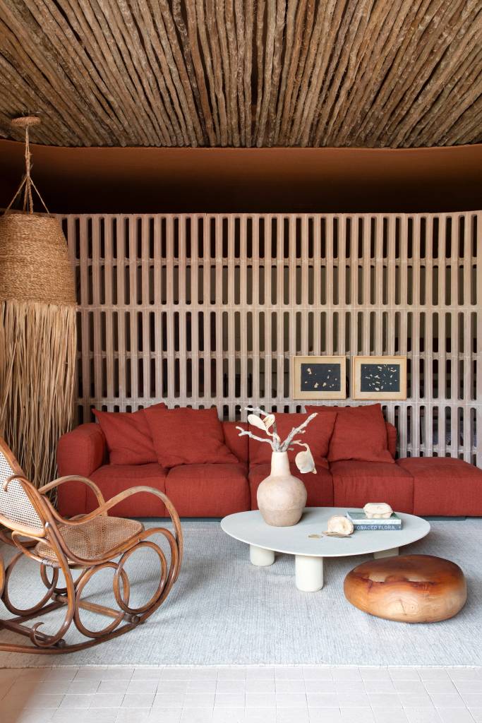 Casa traz paleta em tons terrosos, materiais e plantas inspiradas no cerrado mineiro. Projeto de Natália Lemos para a CASACOR Rio 2024. Na foto, sala, sofá vermelho terroso, elemento vazado.