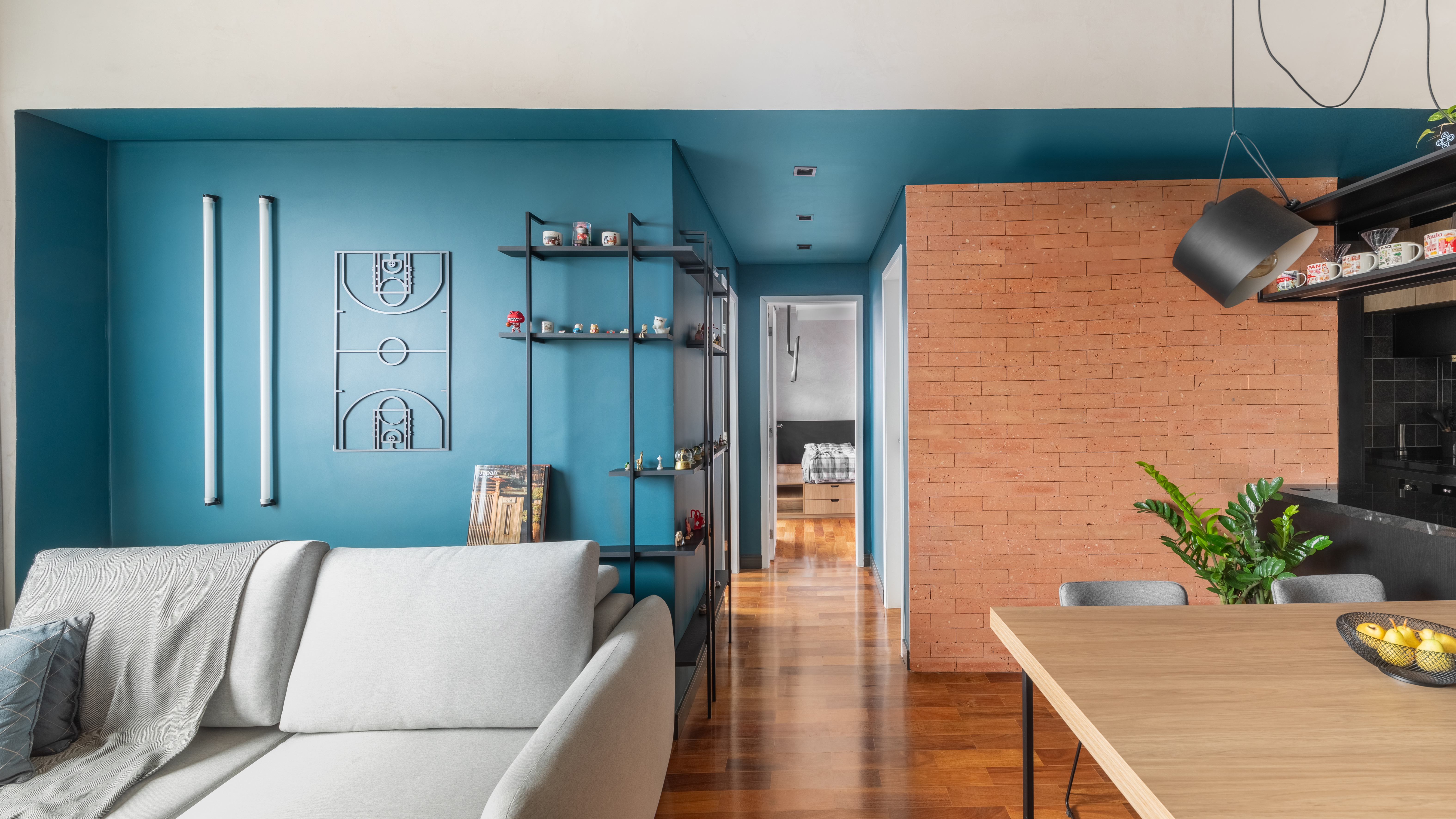 Industrial e leve: apartamento combina serralheria com cores claras e escuras. Projeto de Studio Elã. Na foto, sala, parede azul, estante de serralheria, sofá cinza, tijolinhos.