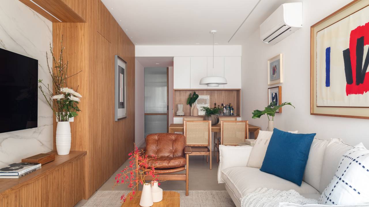 Novo lar de mãe e filha tem espaço de home office e estante de marcenaria ripada. Projeto de Carmen Zaccaro. Na foto, sala de estar integrada com jantar, sofá branco.