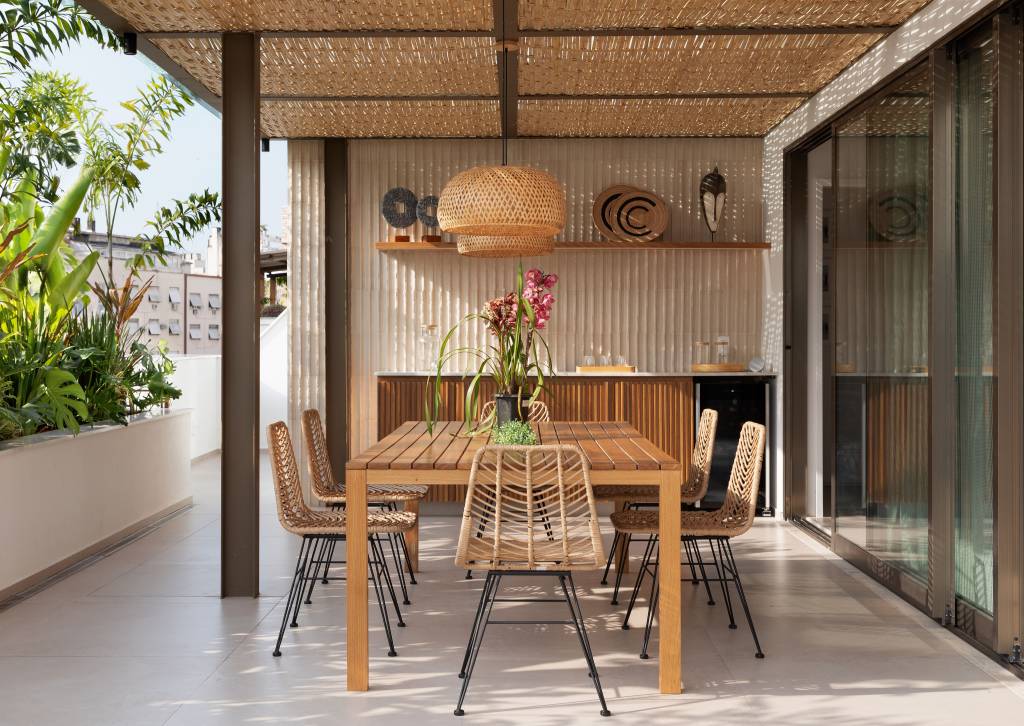 Pergolado com forro de bambu cria área de apoio charmosa para cozinha gourmet. Projeto de House in Rio Arquitetura. Na foto, varanda, mesa de madeira, luminária de palhinha.