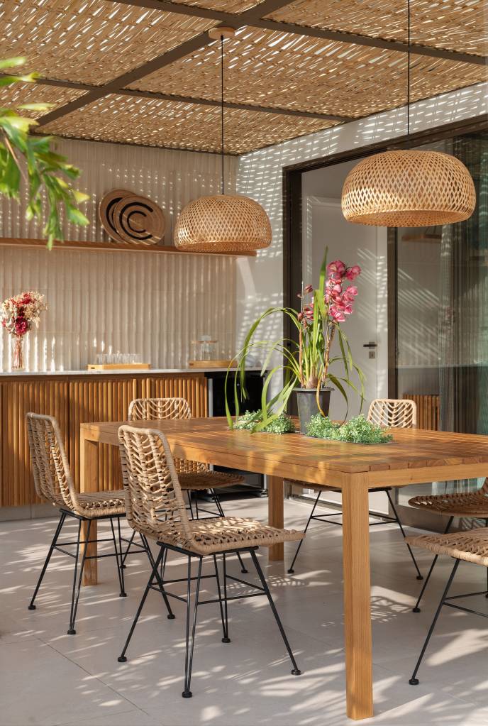 Pergolado com forro de bambu cria área de apoio charmosa para cozinha gourmet. Projeto de House in Rio Arquitetura. Na foto, varanda, mesa de madeira, luminária de palhinha.