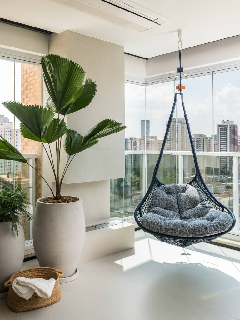 Apartamento pensado para receber com conforto tem toques de azul e mostarda. Projeto de Tetriz Arquitetura. Na foto, varanda, balanço suspenso, plantas.
