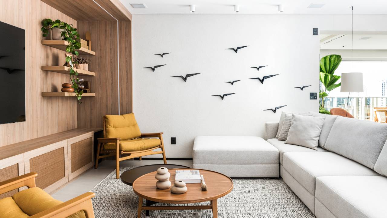 Apartamento pensado para receber com conforto tem toques de azul e mostarda. Projeto de Tetriz Arquitetura. Na foto, sala de estar, poltrona amarela, pássaros decorativos na parede.