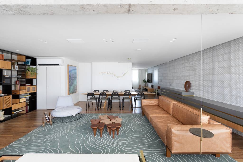 Hall de entrada revestido com muxarabis iluminados são destaque em apartamento. Projeto de Zalc Arquitetura. Na foto, sala de estar, sofá em couro, tapete.
