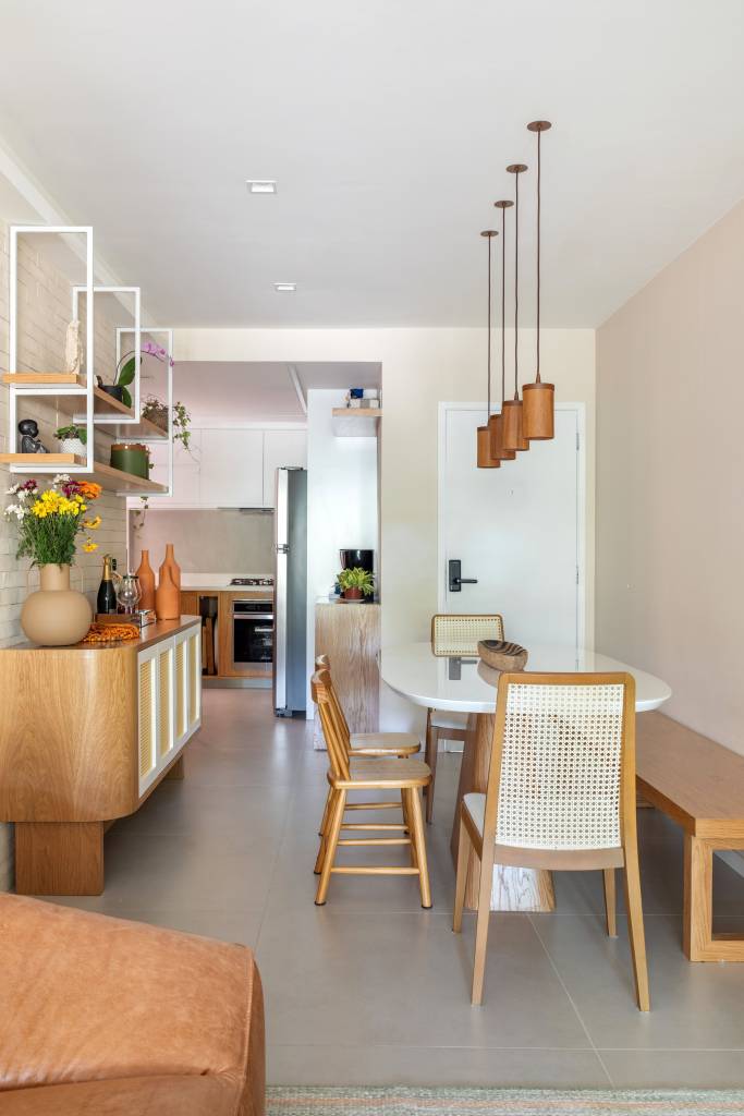 Madeira e palhinha marcam presença nos móveis e marcenaria de apê de 100 m². Projeto de Co+Lab Juntos Arquitetura. Na foto, sala de jantar estreita com banco.