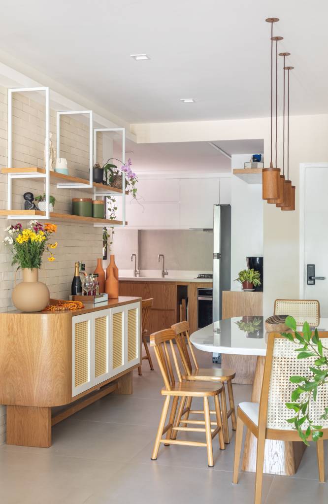 Madeira e palhinha marcam presença nos móveis e marcenaria de apê de 100 m². Projeto de Co+Lab Juntos Arquitetura. Na foto, sala de jantar estreita com banco, buffet.