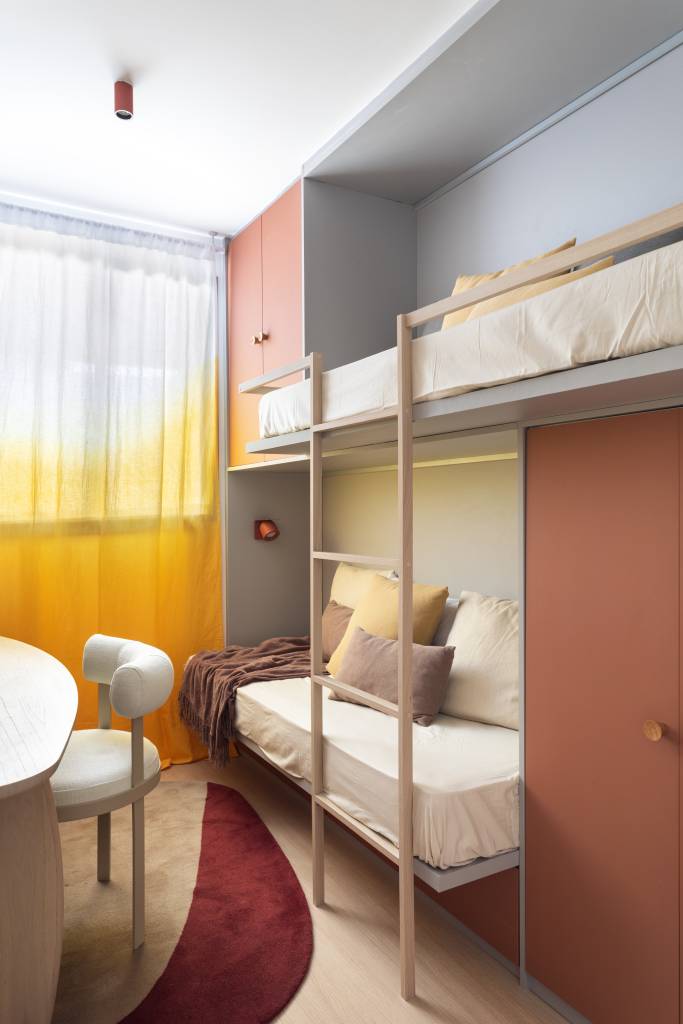 Apê neutro e compacto de 55 m² tem uma suíte e revestimento cerâmico na sala. Projeto de Studio Leandro Neves. Na foto, quarto infantil, beliche, cortina colorida.