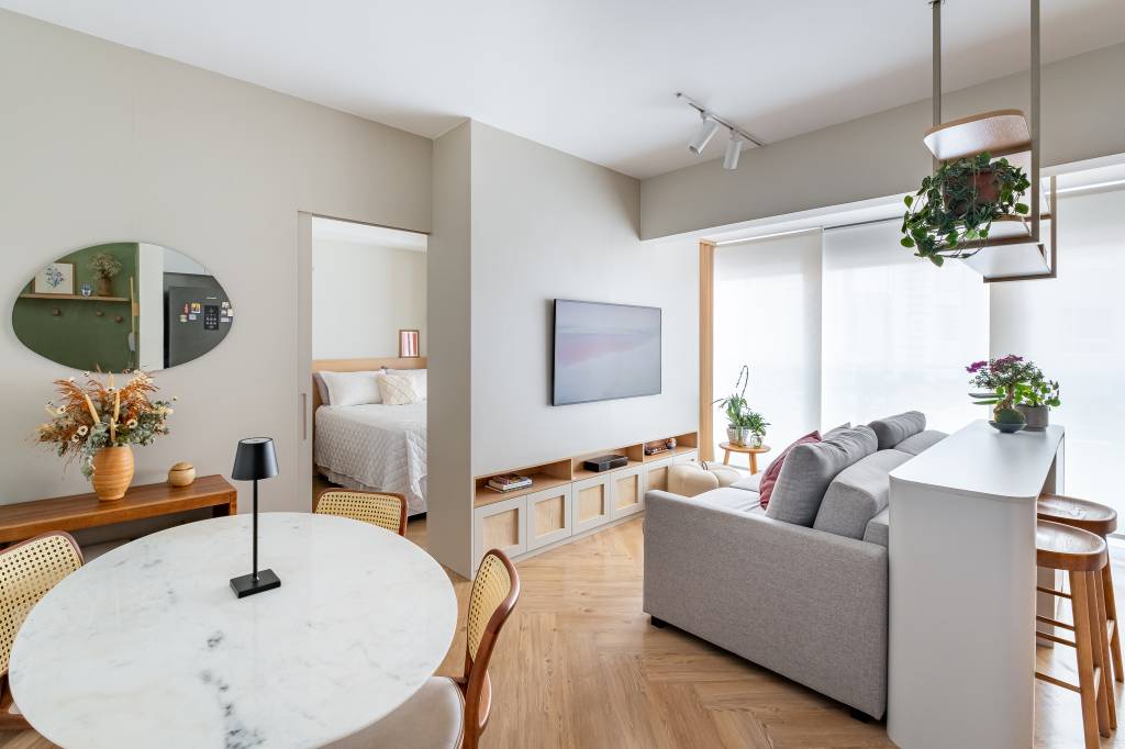 Marcenaria planejada é rack na sala e guarda-roupa no quarto neste apê de 39 m². Projeto de Bya Ribeiro Arquitetura e Thaís Viana. Na foto, sala de estar integrada, sofá cinza, piso espinha de peixe.