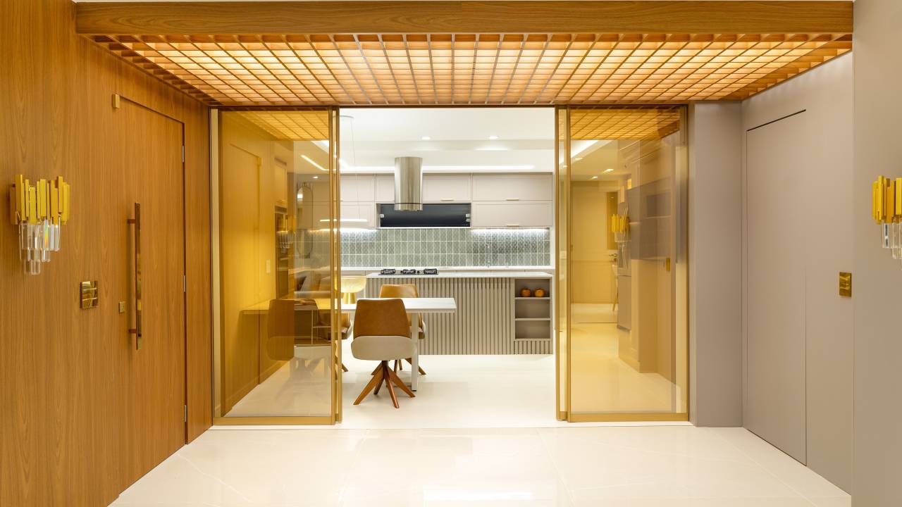 Muxarabi em marcenaria no teto ilumina hall de entrada de apartamento. Projeto de MA.DÊ Arquitetura. Na foto, portas de viro para cozinha.