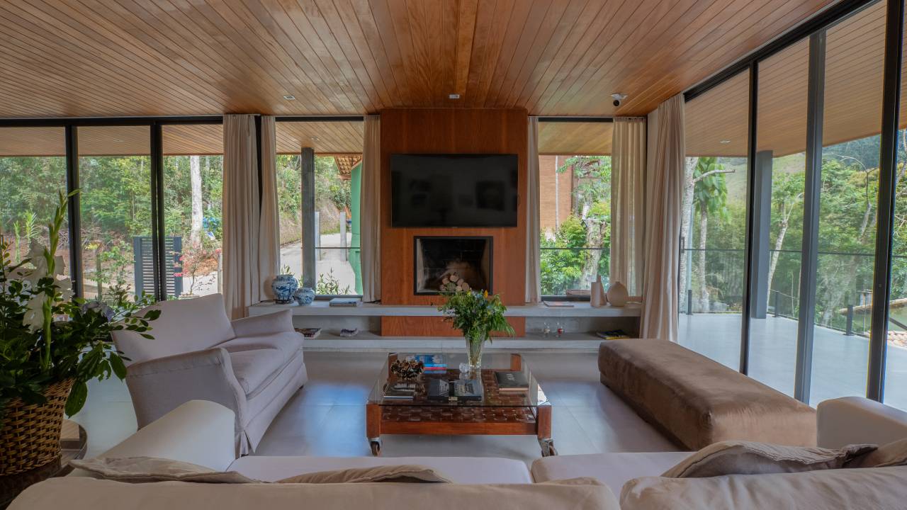 Soluções sustentáveis e vistas exuberantes marcam casa na serra. Projeto de Viviane Cunha. Na foto, sala de estar com lareira.